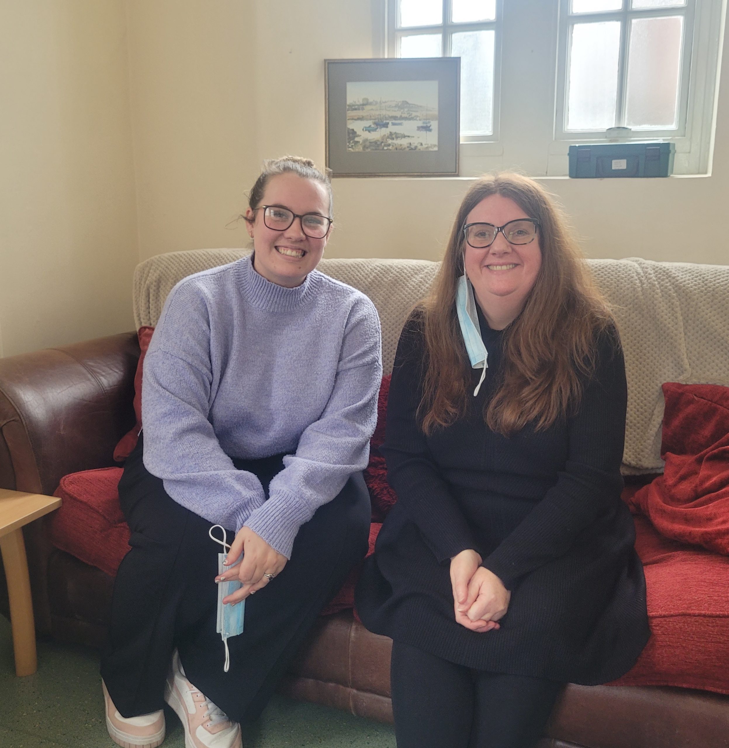 Charley and Suzanne smiling whilst sitting on a sofa